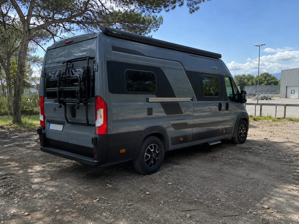 Adria Twin von hinten auf einem Stellplatz unter Bäumen